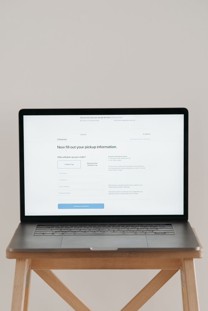 about-us-02 Modern laptop displaying a checkout form against a minimalist beige backdrop.